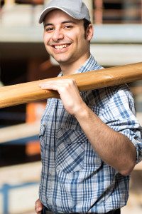 Male Contractor Holding Wood and Smiling at the Camera